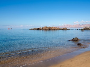 Une plage avec une eau d’un bleu limpide, des formations rocheuses et un bateau qui se dessine à l’horizon.