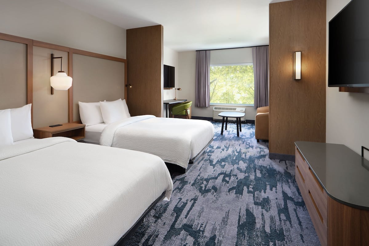 Une chambre d’hôtel avec deux lits, un bureau, une chaise, une télévision et une fenêtre avec des rideaux.