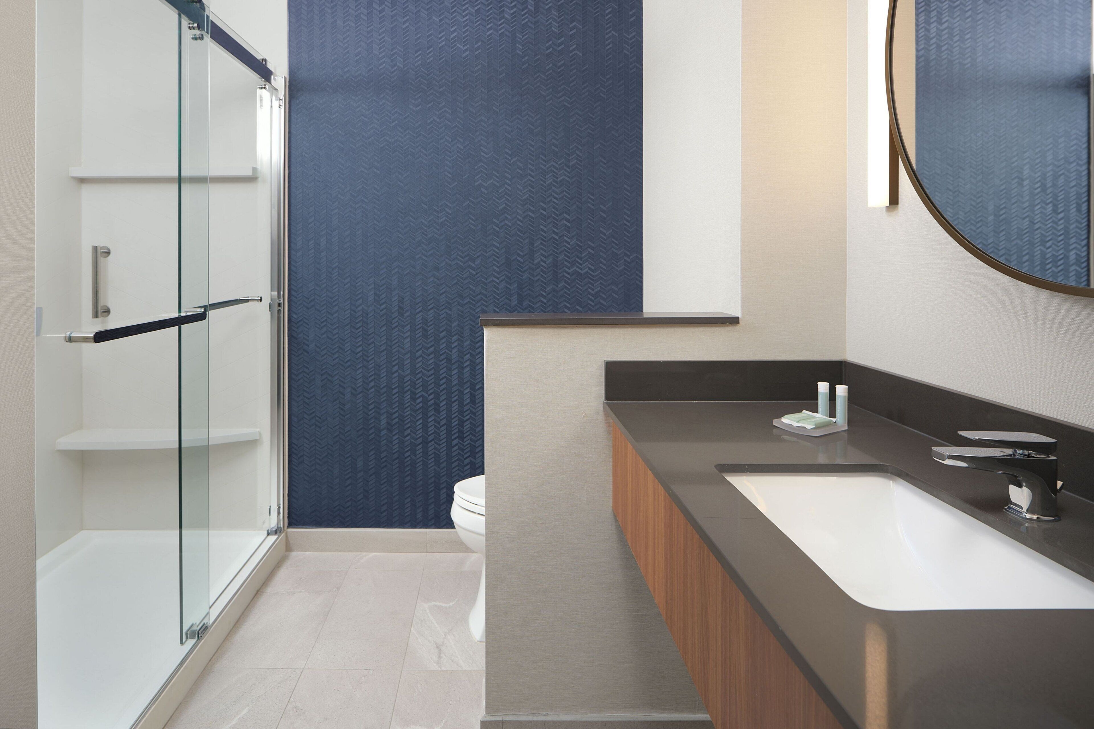 A modern bathroom with a glass shower enclosure, a white sink, and a dark patterned wall.