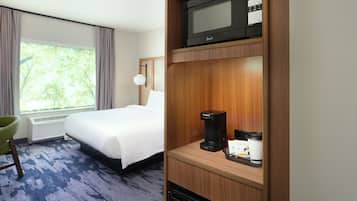 Una habitación de hotel con cama, escritorio con cafetera, microondas y ventana con cortinas.