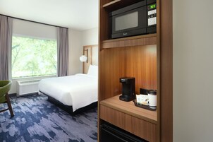 Una habitación de hotel con cama, escritorio con cafetera, microondas y ventana con cortinas.