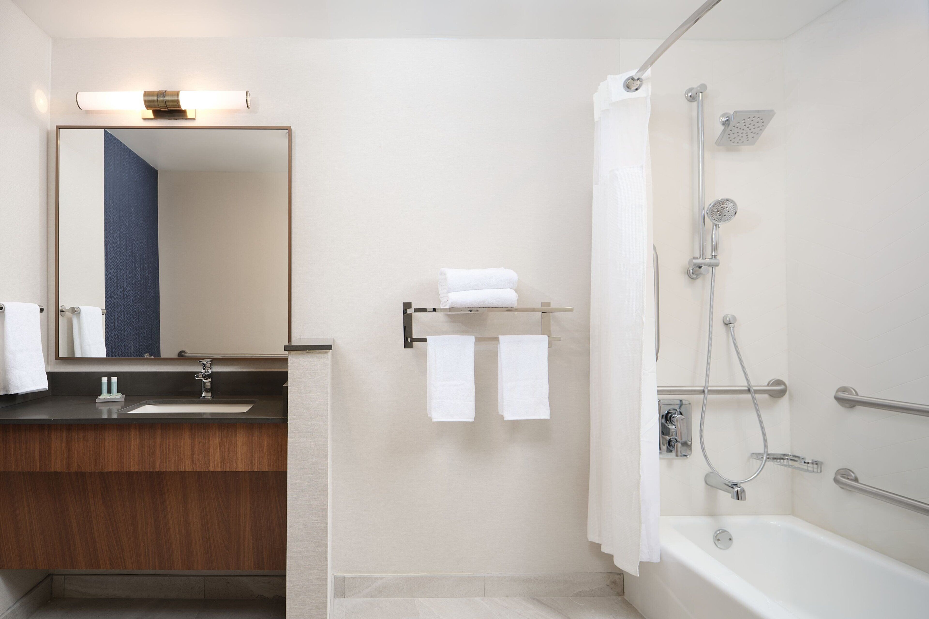 A modern bathroom with a sink, mirror, towel rack, and a walk-in shower with a bathtub.