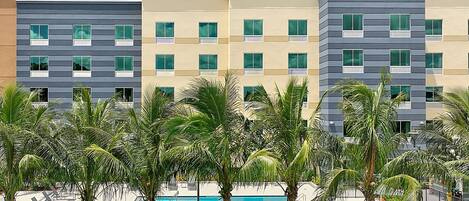 A hotel with multiple floors, a swimming pool, and palm trees in the foreground.