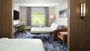Une chambre d’hôtel comprenant un lit, un bureau, une chaise, un canapé, une télévision, une fenêtre avec des rideaux et une lampe.