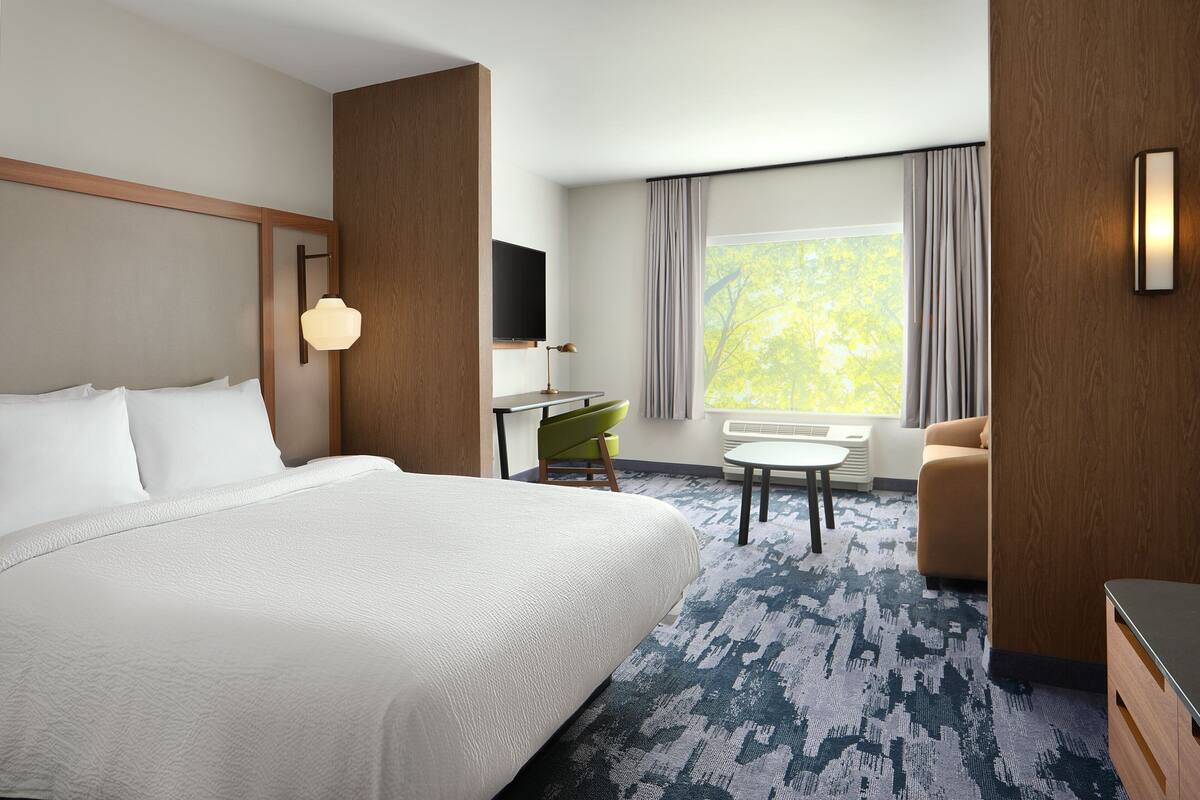 Une chambre d’hôtel avec un grand lit, un bureau avec une chaise, un canapé, un téléviseur fixé au mur et une fenêtre avec des rideaux.