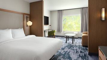 A hotel room with a large bed, a desk with a chair, a sofa, a TV mounted on the wall, and a window with curtains.