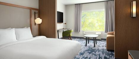 A hotel room with a large bed, a desk with a chair, a sofa, a TV mounted on the wall, and a window with curtains.