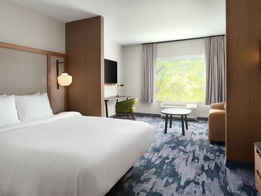 A hotel room with a large bed, a desk with a chair, a sofa, a TV mounted on the wall, and a window with curtains.