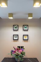 Un mur orné de quatre tableaux représentant des papillons, chacun étant encadré, et une table sur laquelle est posé un vase de fleurs.