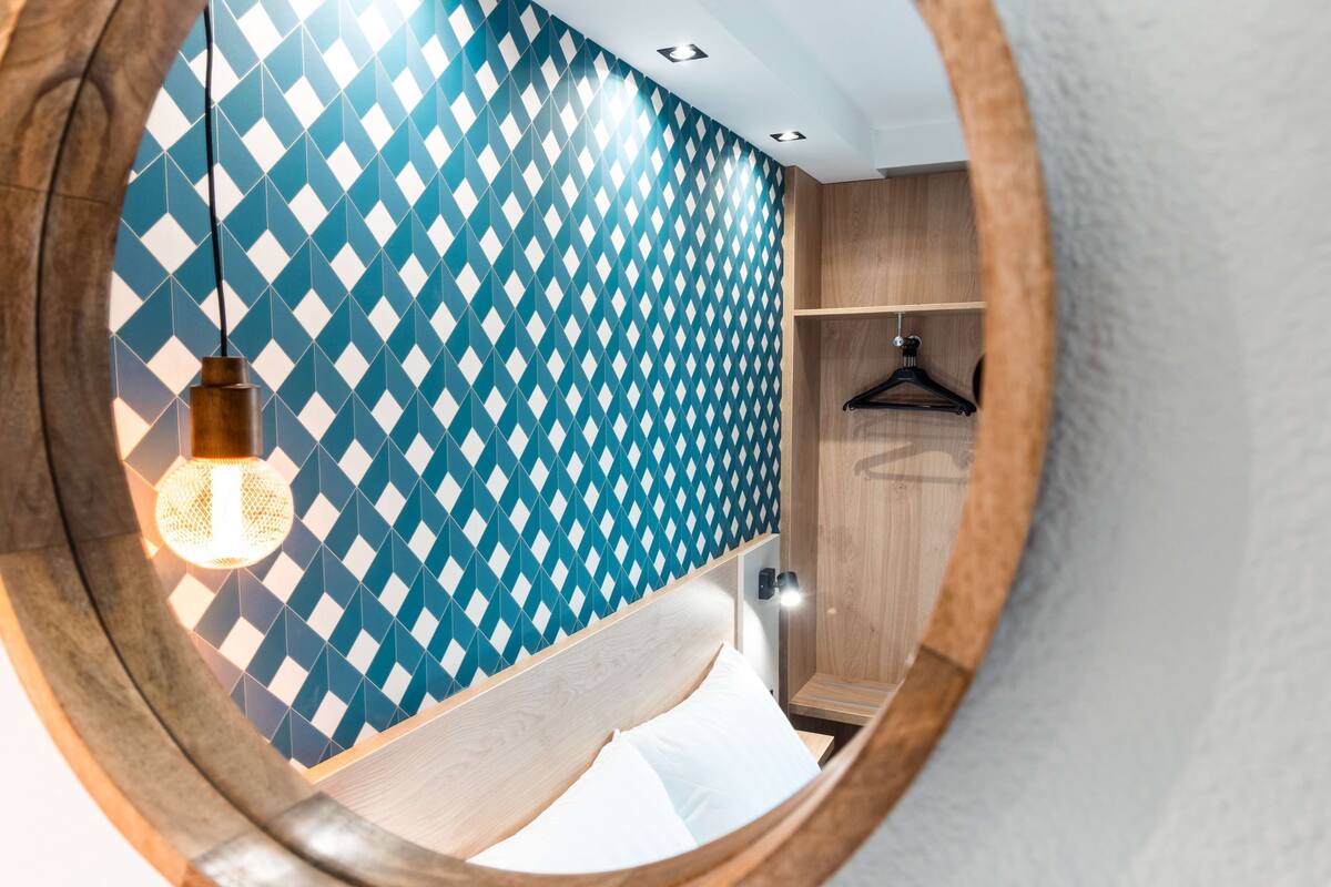 A circular view of a room with a patterned wall, a hanging light fixture, a wooden wardrobe, and a bed with white bedding.