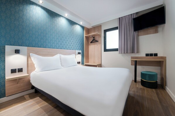 A modern hotel room with a large bed, bedside tables, a TV, and a small desk.