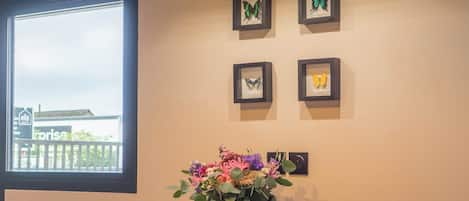 A dining area with a wooden table, two chairs, a vase with flowers, and butterfly wall art.