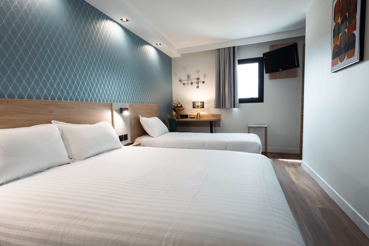 A hotel room with two beds, a small desk, a TV, and a window with curtains.