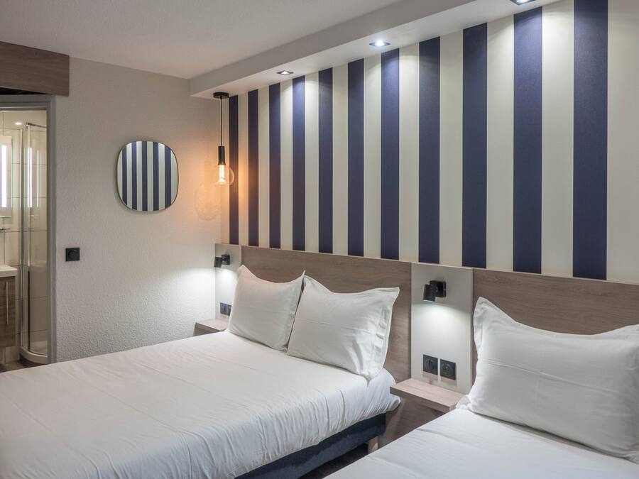 A hotel room with two beds, a large mirror, and a striped wall.