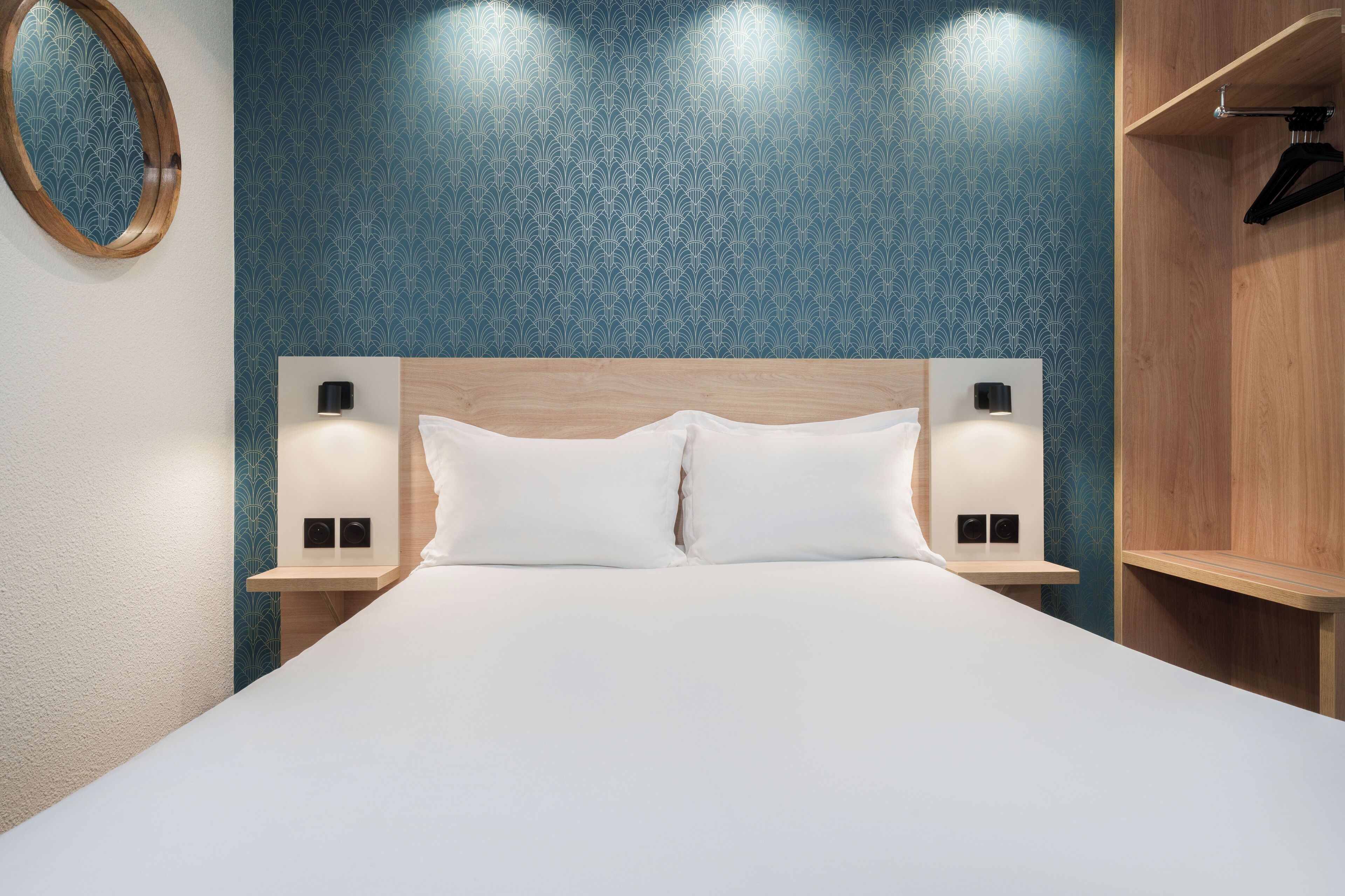 A neatly made bed with white linens, two bedside tables with wall-mounted lamps, and a blue patterned wall.