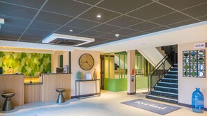 A reception area with a reception desk, a clock, a green wall, and a staircase leading to the upper floor. - Kyriad Direct Orleans Nord - Cap Saran (Saran)