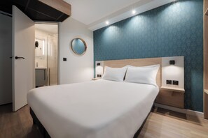 A modern hotel room with a large bed, a wooden headboard, a round mirror, and a built-in nightstand. - Kyriad Direct Orleans Nord - Cap Saran (Saran)