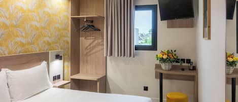 Una habitación de hotel con cama, escritorio con televisor, ventana y planta.