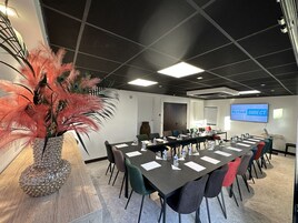 Une salle de conférence avec une longue table, des chaises, une plante décorative et un écran affichant le logo « Kyriad DIRECT ».