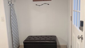 Ein kleiner, sauberer Raum mit einem schwarzen Hocker, einem gerahmten Bild an der Wand und einer Tür mit Fenster.