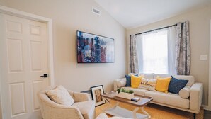 Un salon avec un canapé, des fauteuils, une table basse et un tableau représentant un paysage urbain accroché au mur.