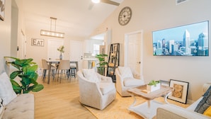 Un vaste salon doté d’un téléviseur diffusant des images de la ville, un coin repas et une cuisine en arrière-plan.