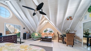 A spacious attic bedroom with a large bed, a ceiling fan, a sofa, and a dining table. - Gate House; a Private Villa within a Luxurious Estate near world-class fishing (Marsh Harbour)