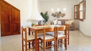 Een eetgedeelte met een houten tafel en stoelen, een bank, decoratieve wandkunst en een groot raam met uitzicht.
