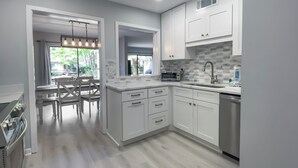 A modern kitchen with white cabinetry, a built-in oven, and a window overlooking a garden.