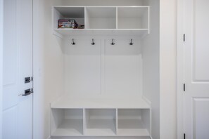 Un armario blanco con estantes y ganchos, una puerta con manija, y una caja pequeña en el estante superior.