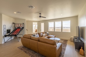 A living room with a brown leather sofa, a small coffee table, a TV stand, and a ceiling fan. - Desert Retreat (St. George)