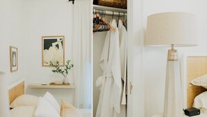 Une chambre à coucher avec un lit, une table de chevet avec une lampe, une commode, une armoire avec des vêtements suspendus et un tableau encadré au mur.