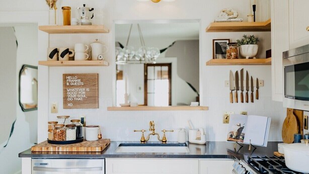 Une cuisine avec des étagères en bois, un îlot central et un panneau fixé au mur.
