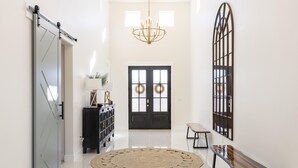 A hallway with a sliding door, a bench, a round rug, a chandelier, and a door with wreaths. - Colombia Retreat (St. George)