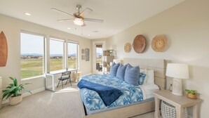 Ein Schlafzimmer mit Bett, Schreibtisch, Stuhl, Deckenventilator und großen Fenstern.