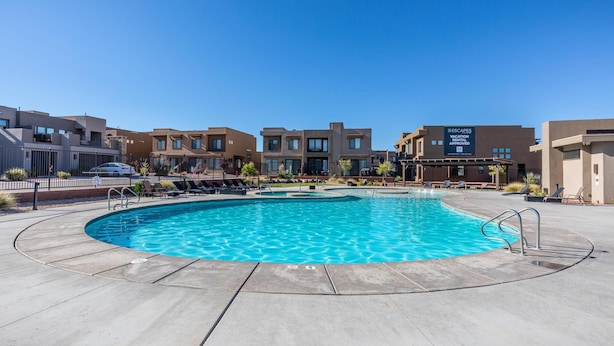 A swimming pool with a clear blue water, surrounded by a concrete deck and lounge chairs. - Poolside Plunge (St. George)