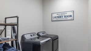 Sala de lavandería automática con dos lavadoras, un tendedero y un letrero que indica servicio las 24 horas.