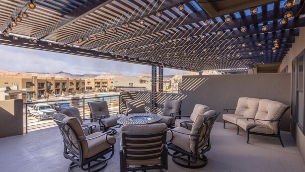 Un espacio de estar al aire libre cubierto con sillas y una mesa, con vistas a una piscina y edificios.