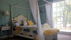 A four-poster bed with a quilt, a bedside table with a lamp, and a window with curtains. - Charming 1940s Home (Jefferson)