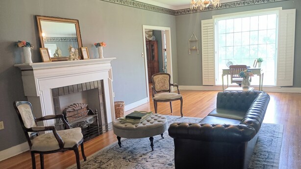 A living room with a fireplace, a sofa, two armchairs, a rug, and a chandelier. - Charming 1940s Home (Jefferson)