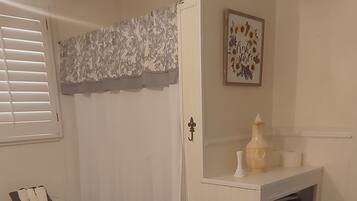 A bathroom with a toilet, a sink, a shelf with towels, a shower curtain, and a framed picture on the wall.