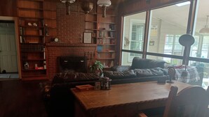 A cozy living room with a fireplace, a leather sofa, a wooden coffee table, and a bookshelf filled with books. - Charming 1940s Home (Jefferson)