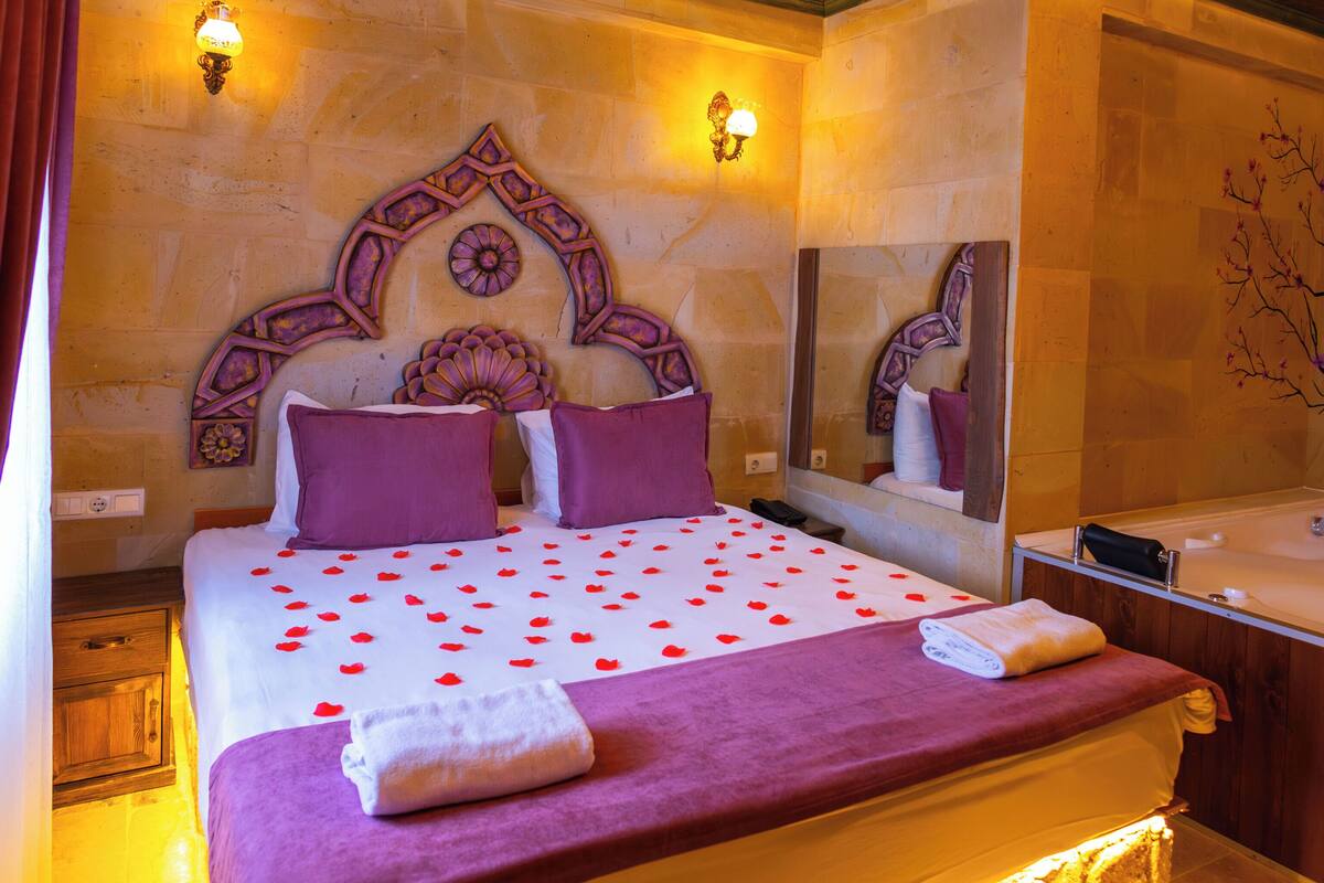 Un dormitorio bien iluminado con una cama grande, cabecera de madera, un espejo y un baño con bañera.