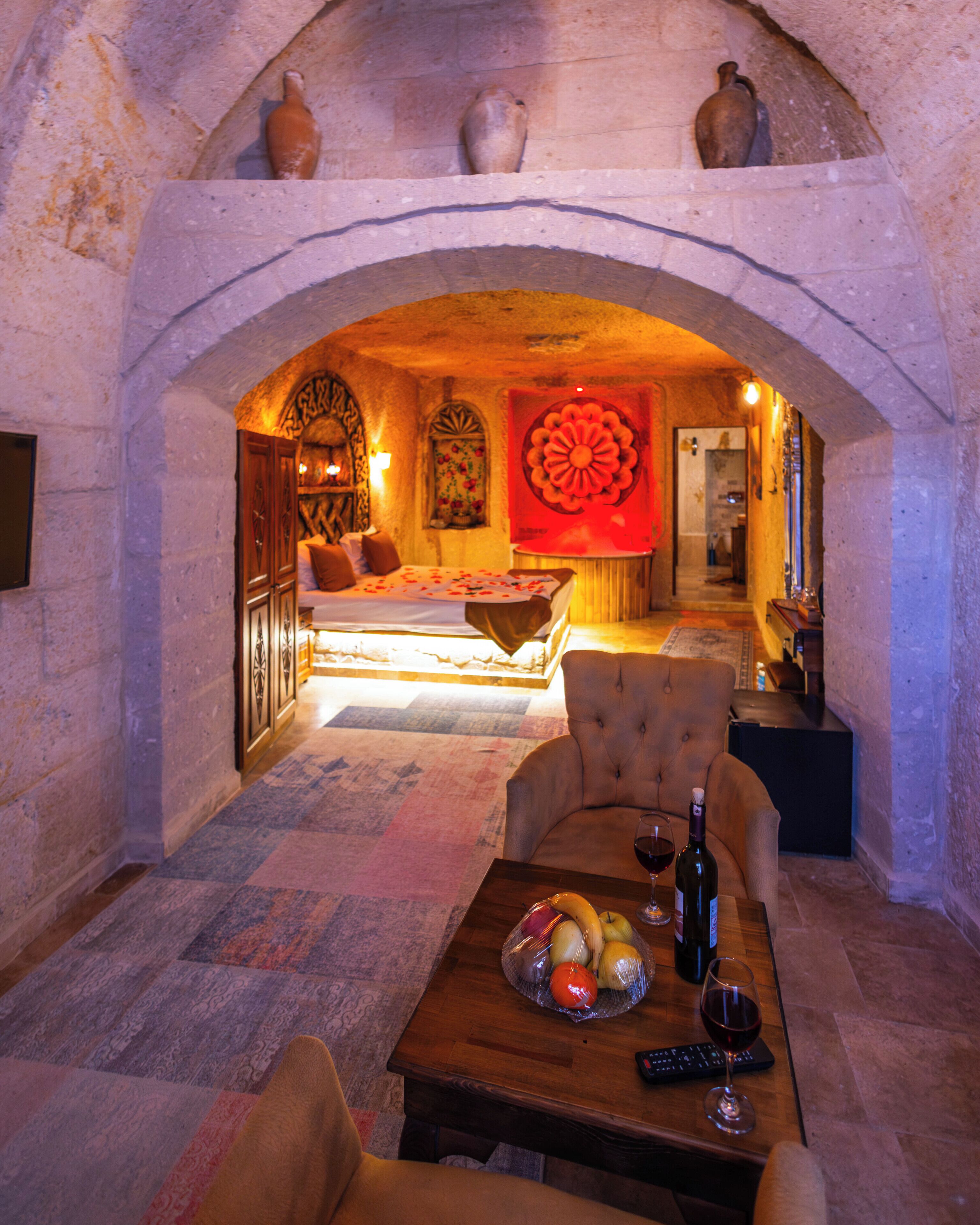 An underground room with a bed, a table with fruit and wine, and a sofa.