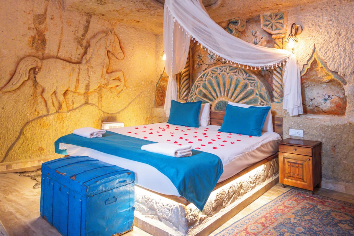 Una habitación con una cama, una mesita de noche, una maleta azul y un tapete estampado.