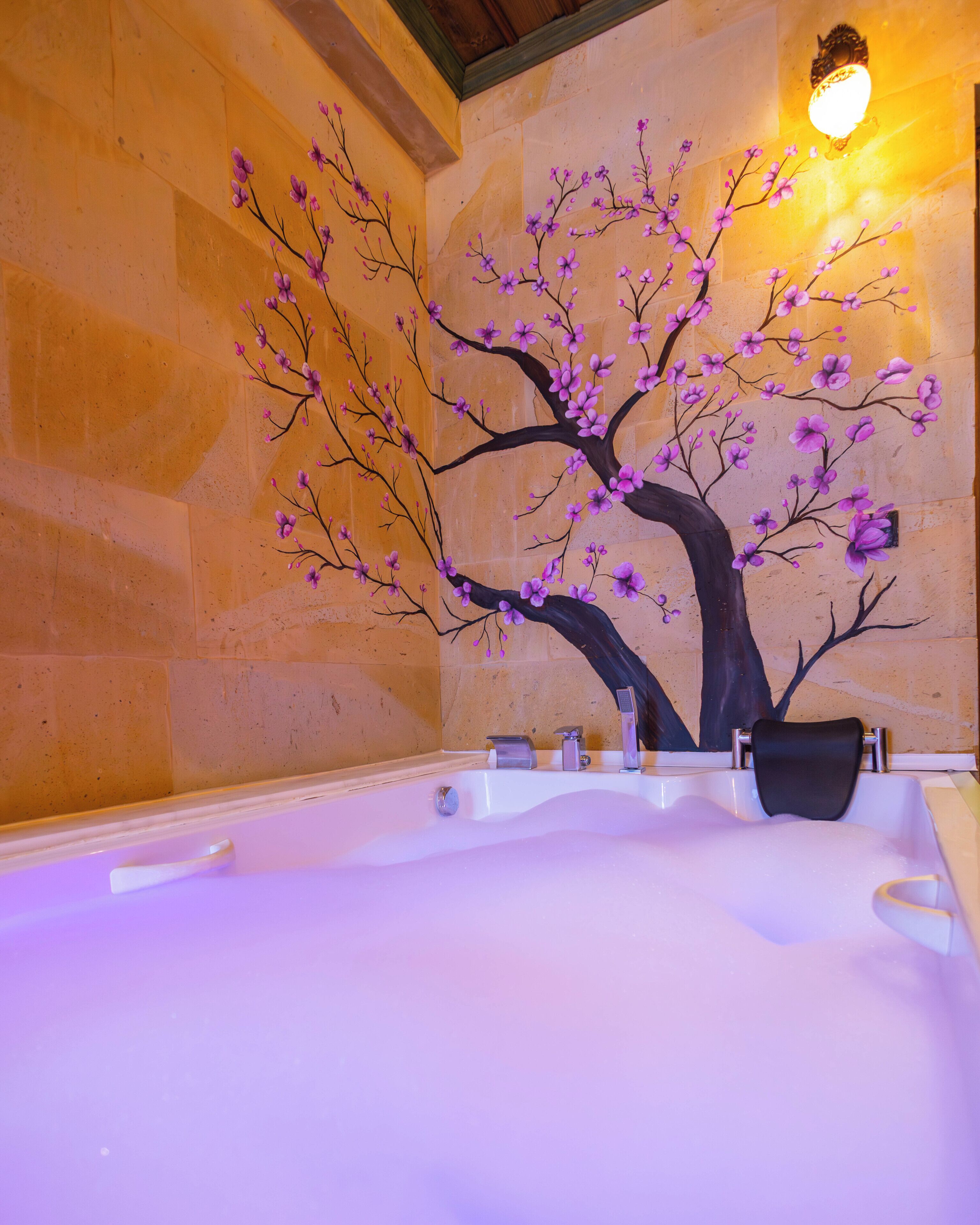 A bathroom with a large bathtub, a wall-mounted light fixture, and a decorative tree mural.