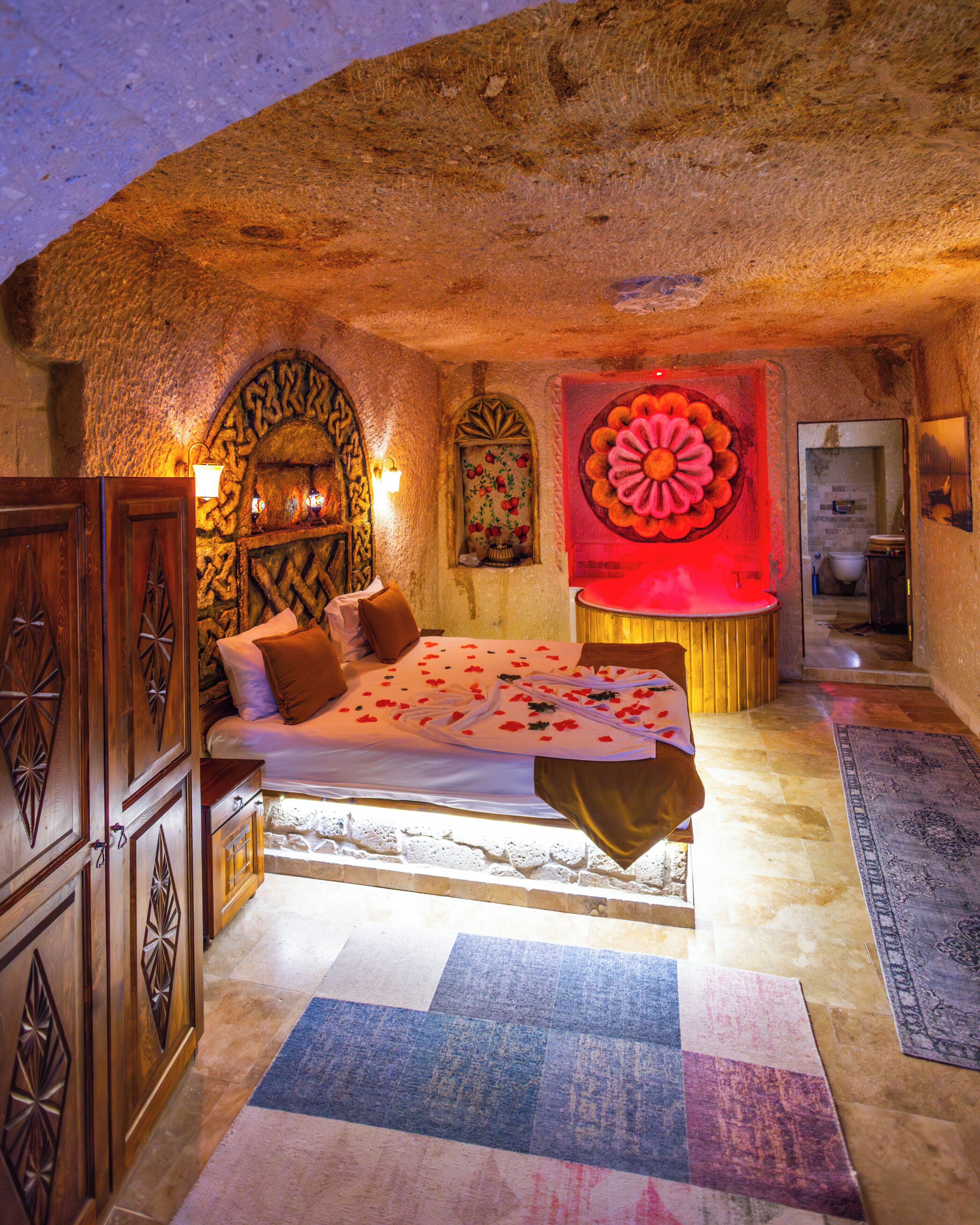 A bedroom with a bed, wooden furniture, a decorative wall, and a bathroom visible through an archway.