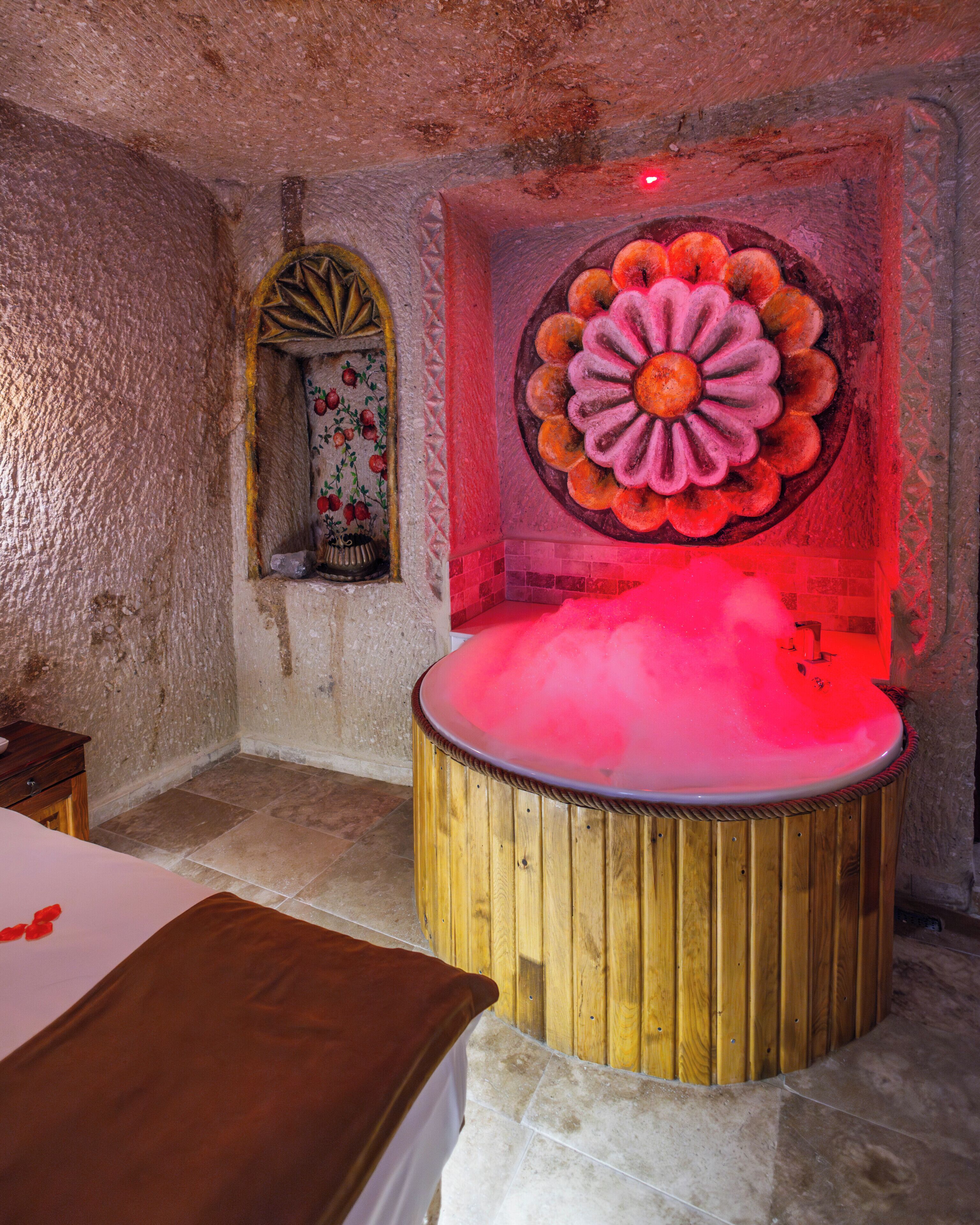A room with a wooden bathtub, a stone wall, and a decorative flower mural.