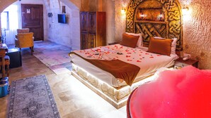 Een slaapkamer met een stenen muur, een bed met rozenblaadjes, een rood bad en een houten deur.