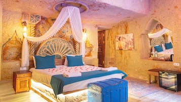 Un dormitorio con cama con dosel, una mesita de noche, una pequeña mesa, un aparador azul y una alfombra estampada.